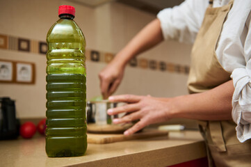 Plastic bottle of green liquid, possibly cooking oil, sitting on a kitchen counter. In the...
