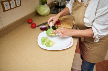 Woman preparing fresh avocado slices in kitchen