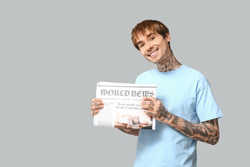 Handsome young man with newspaper on grey background