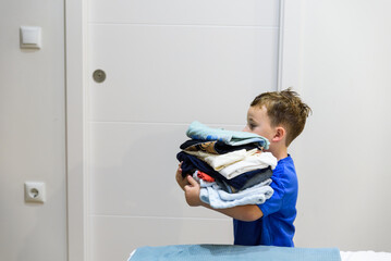 Young child carrying stack of folded clothes, helping with laundry chores