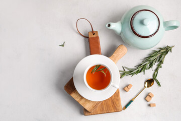 Wooden board with cup and teapot of hot rosemary tea on white background