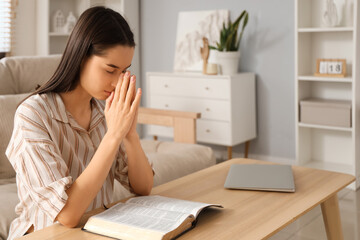 Beautiful young woman reading Bible and praying at home