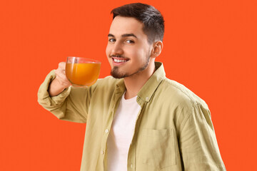 Fototapeta premium Young man with cup of lemon tea on orange background