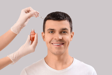 Young man with hair loss problem receiving treatment on light background, closeup