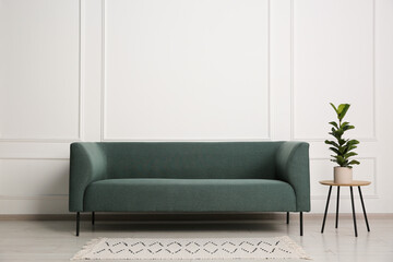 Stylish sofa and side table with houseplant near white wall indoors