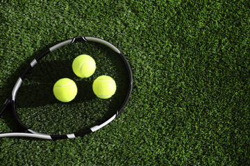 Tennis racket and balls on green artificial grass, flat lay. Space for text