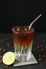 Refreshing espresso tonic drink with slice of lime and coffee beans on dark table