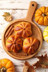Tasty pumpkin shaped buns, ingredients and dry leaves on old wooden table, flat lay