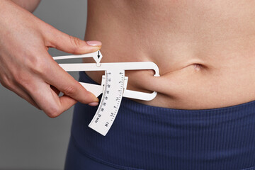 Woman measuring body fat with caliper on gray background, closeup