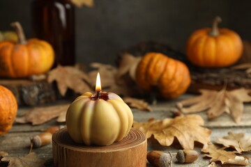 Autumn atmosphere. Burning pumpkin shaped candle and dry leaves on wooden table, closeup