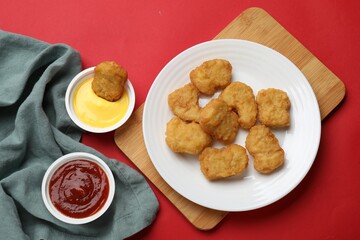 Delicious chicken nuggets and sauces on red background, flat lay