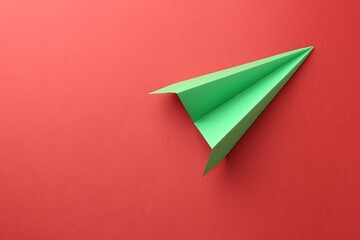 One handmade green paper plane on red background, top view. Space for text