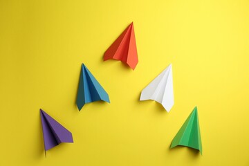 Handmade color paper planes on yellow background, flat lay