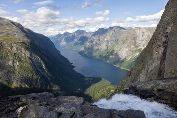 View of the landscape with the source of the Mardalsfossen waterfall in Norway. Grey sky with clouds, grey mossy rocks, white water of the waterfall and dark blue Eikesdalsvatnet lake