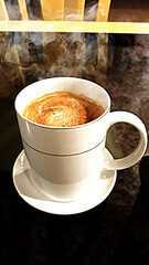 Large cup of hot, steaming coffee and small saucer.