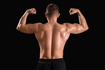 Male bodybuilder showing muscles on dark background, back view