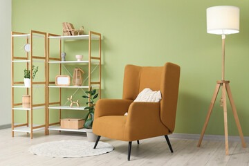 Shelving units and comfortable armchair near green wall in interior of living room