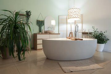 Interior of bathroom with bathtub, plants and glowing lamps in evening