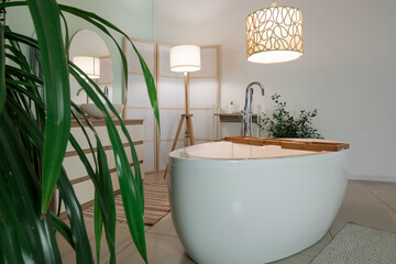 Interior of bathroom with bathtub, folding screen and glowing lamps in evening