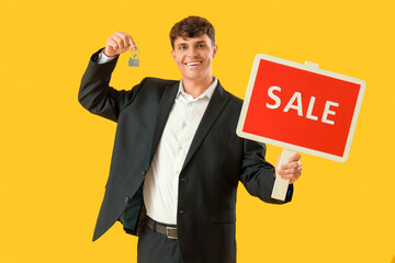 Male real estate agent with key from house and SALE sign on yellow background