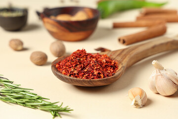 Wooden spoon with chili flakes, garlic and rosemary on color background, closeup