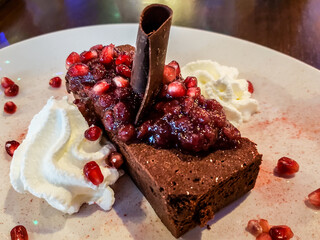 Delicious dessert – a slice of a brownie on a white plate with pomegranate seeds, homemade...
