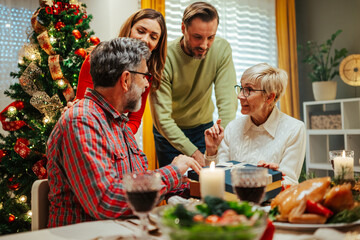 Family giving christmas gift to senior woman at dinner table