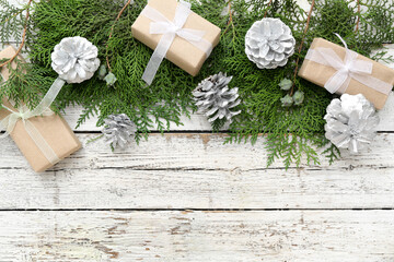 Christmas composition with thuja branches, silver cones and gifts on white wooden background. Top...