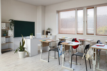 Interior of empty classroom with school desks and greenboard