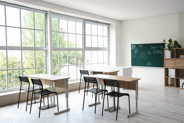 Interior of empty classroom with school desks and text BACK TO SCHOOL on chalkboard