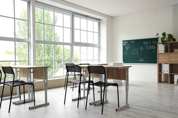 Interior of empty classroom with school desks and text BACK TO SCHOOL on chalkboard