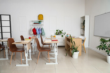 Interior of empty classroom with school desks, whiteboard and backpacks hanging on hooks