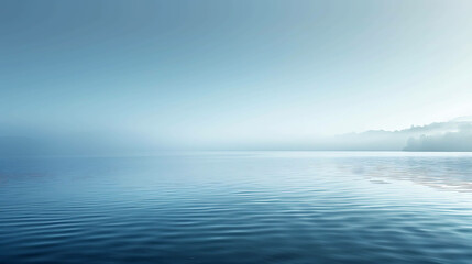 Obraz premium This is a beautiful misty lake landscape. The water is a deep blue color and the sky is a light blue color.