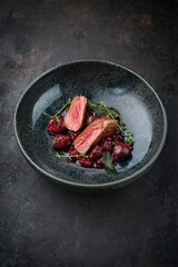 Traditionally roasted fillet of saddle of venison with chestnuts, bacon-wrapped bean sticks and redcurrants served with lingonberry sauce as close-up in a bowl with a rustic background