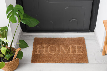 Brown door mat with word HOME and houseplant near black door. Closeup