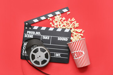 Movie clapper with film reels and popcorn on red background