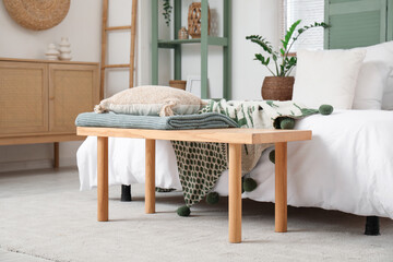 Bench with pillow and plaid near comfortable bed in interior of bedroom