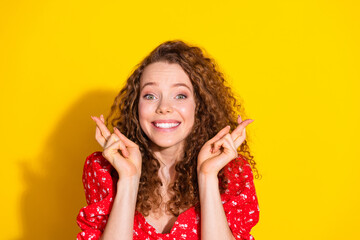 Photo of adorable excited girl wear red top fingers crossed empty space isolated yellow color...