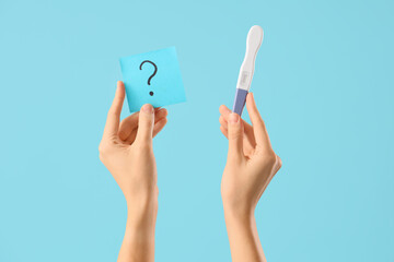 Female hands with pregnancy test and paper with question mark on blue background. Closeup
