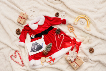 Composition with baby Santa costume, sonogram, pregnancy test and Christmas decor on white fabric...