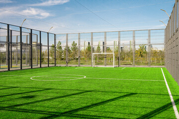 An empty green outdoor soccer field with artificial turf, fenced with a metal fence, for outdoor sports and training © YuTphotograph
