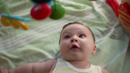 Baby lying on a play mat, wide-eyed while observing colorful hanging toys, playful and engaged in sensory development, early childhood discovery in a home setting