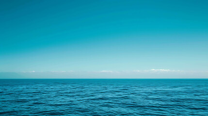 Deep blue ocean with a clear blue sky and distant clouds. The water is calm and serene, with gentle waves rippling across the surface.