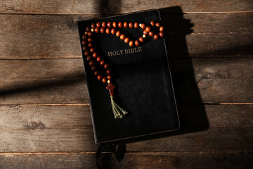 Holy Bible with rosary beads on wooden background