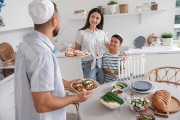 Happy family having dinner with potato pancakes and tasty donuts in festive kitchen. Hanukkah celebration