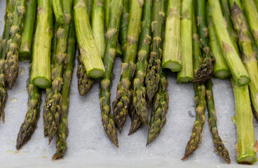Nahaufnahme von dem im Ofen gebratenen Spargel mit Salz und Olivenöl auf dem Ofenblech mit Backpapier. Aufnahme von vorne.
