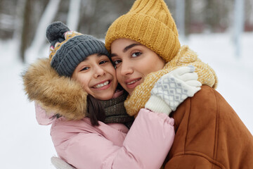 Portrait of happy young mother and daughter embracing playfully and looking at camera having fun in winter outdoors