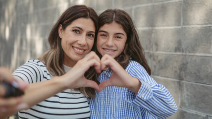 We love you. Latin mom and preteen daughter video bloggers influencers shoot content unite fingers in heart sign grateful for attention. Bonding mother and kid shoot selfie look at camera express love