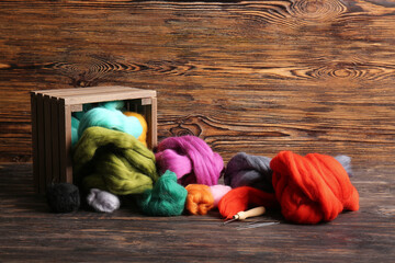 Overturned basket with different wool for felting and needles on wooden background