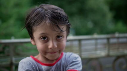 Young boy standing on a balcony, playful and cheerful, engaging with the camera, fun and energetic moment in an outdoor setting with natural surroundings